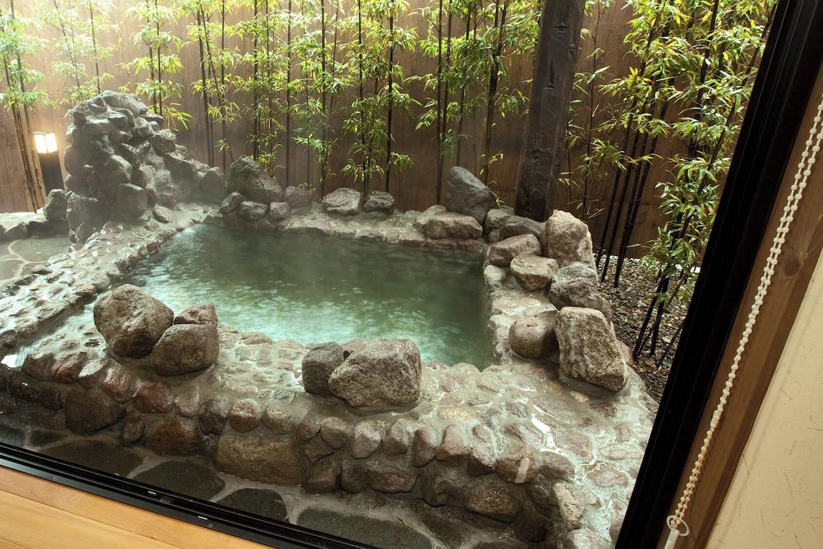A rock-lined hot spring surrounded by bamboo plants.