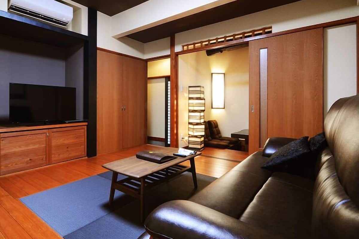 A living room with a leather sofa, a TV, a coffee table, and a bookshelf.