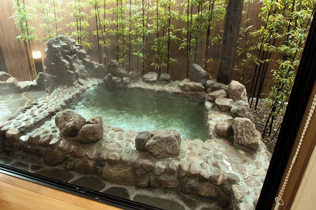 A rock-lined hot spring surrounded by bamboo plants.