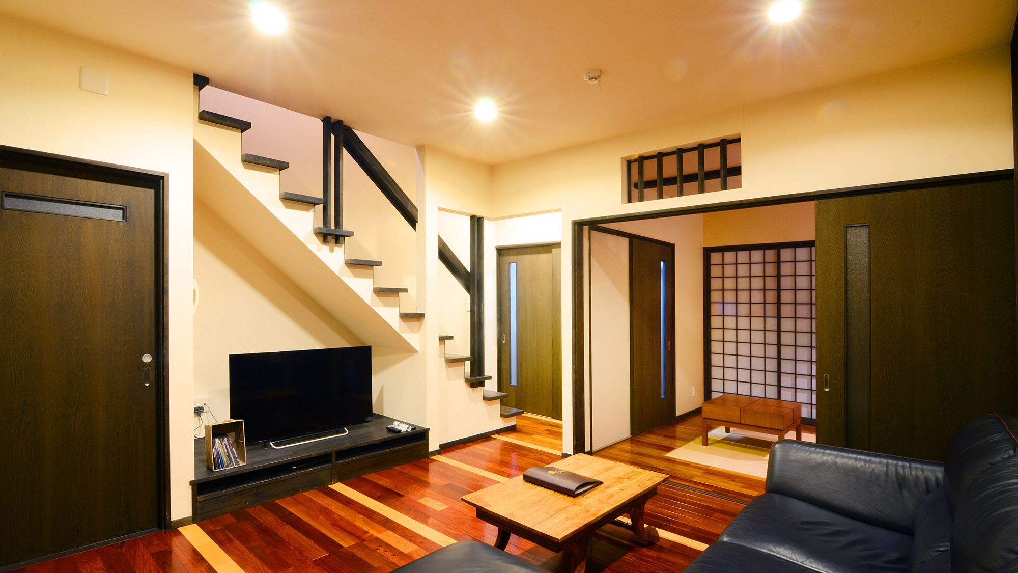 A living room with a TV, wooden flooring, a sofa, a coffee table, and a staircase.