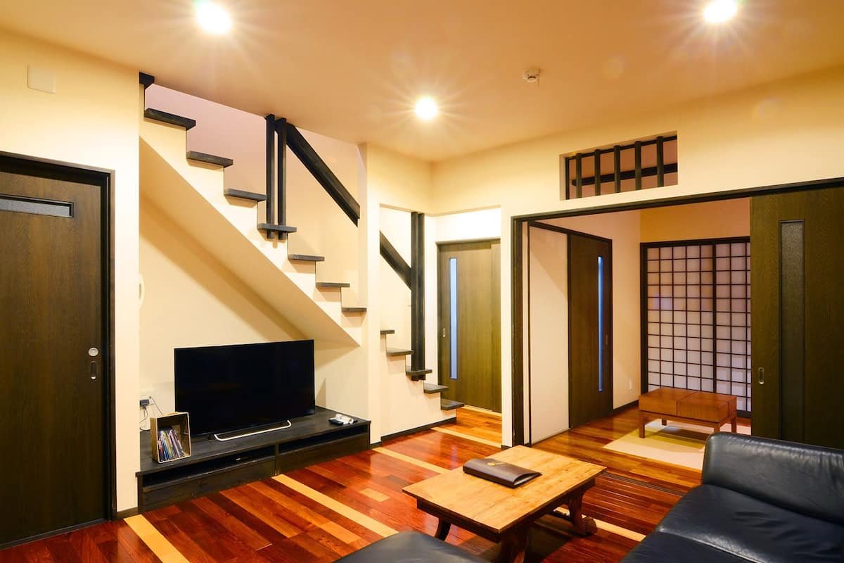 A living room with a TV, wooden flooring, a sofa, a coffee table, and a staircase.