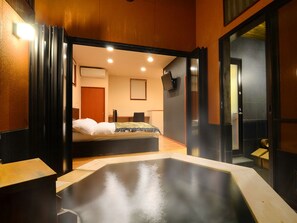A modern hotel room with a large bathtub, a bed, and a desk area. - Tokunoyado Fubuan (Beppu)