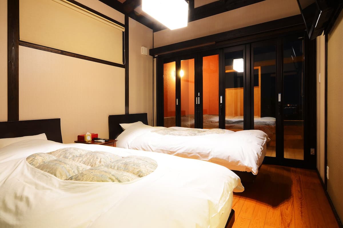 A hotel room with two beds, a sliding glass door leading to a balcony, and a traditional Japanese-style sliding door.