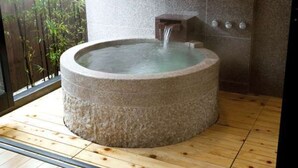 A stone hot tub with a water spout, set on a wooden floor with a bamboo backdrop. - Tokunoyado Fubuan (Beppu)