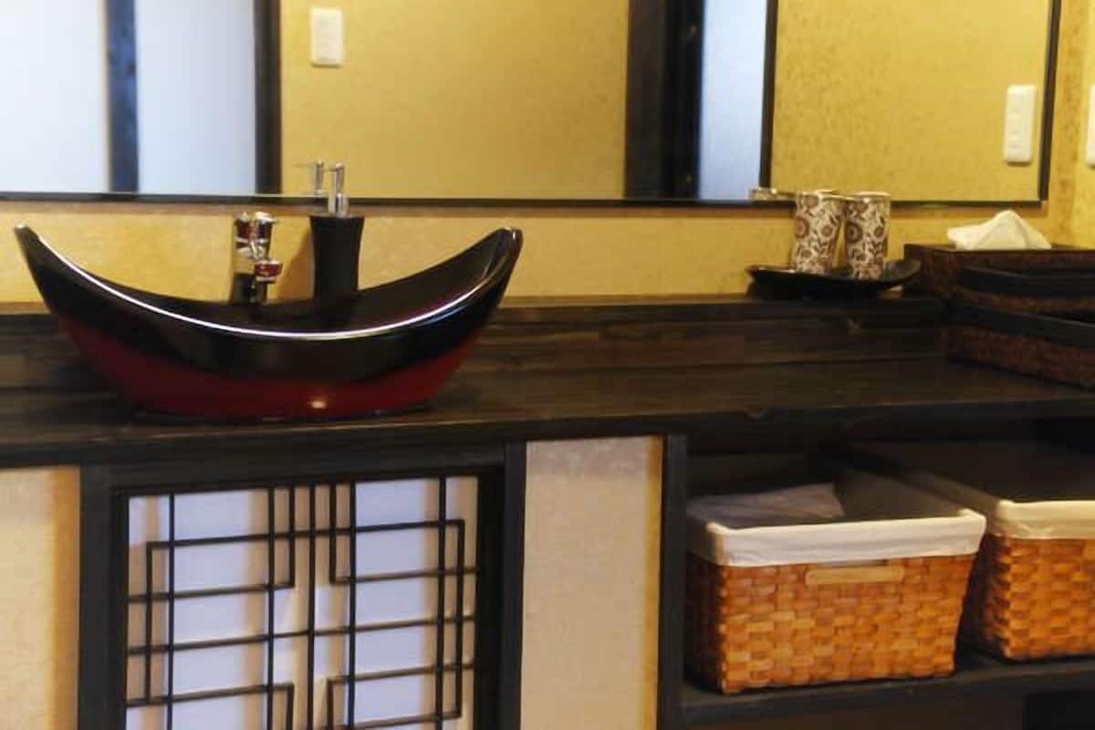 A bathroom with a black and red vessel sink, a mirror, and a traditional Japanese screen.