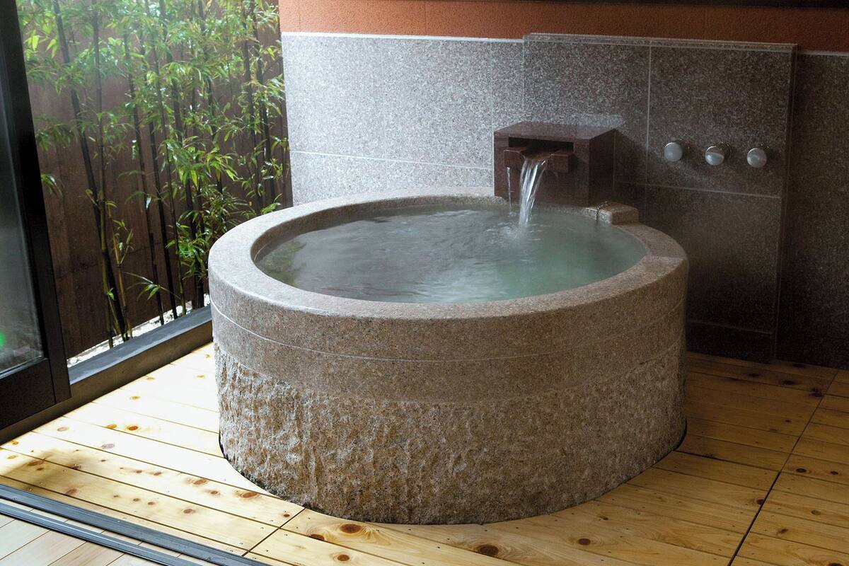 A stone hot tub with a waterfall feature, set on a wooden floor with a bamboo backdrop.