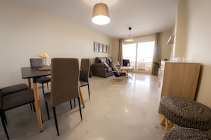 Ein modernes Wohnzimmer mit Essbereich, einer Couch und einem Couchtisch. Es gibt Stühle und eine Lampe.