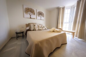 A bedroom with a large bed, a bedside table, a small stool, and two wall-mounted paintings. - Apartamentos Puerto Almerimar (El Ejido)