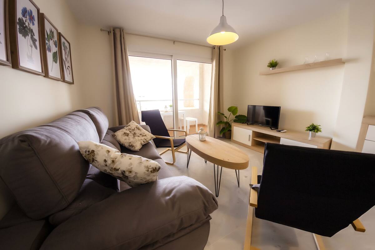 Un salon moderne avec un canapé, une petite table, un fauteuil, un téléviseur et un balcon offrant une vue agréable.