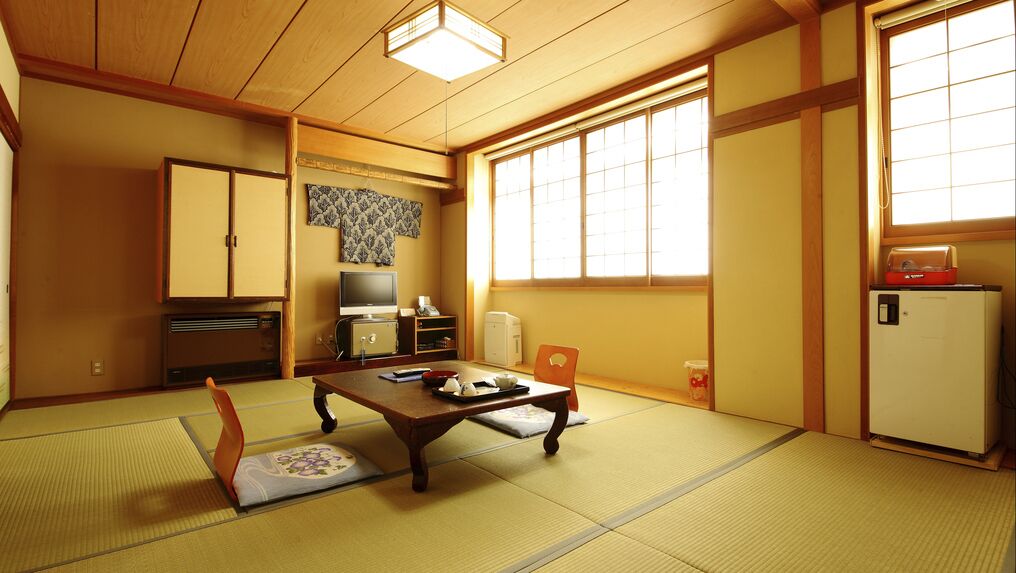 Une pièce de style japonais traditionnel, avec un sol recouvert de tatamis, une petite table basse sur laquelle est posé un plateau, une télévision, un réfrigérateur et des portes coulissantes.