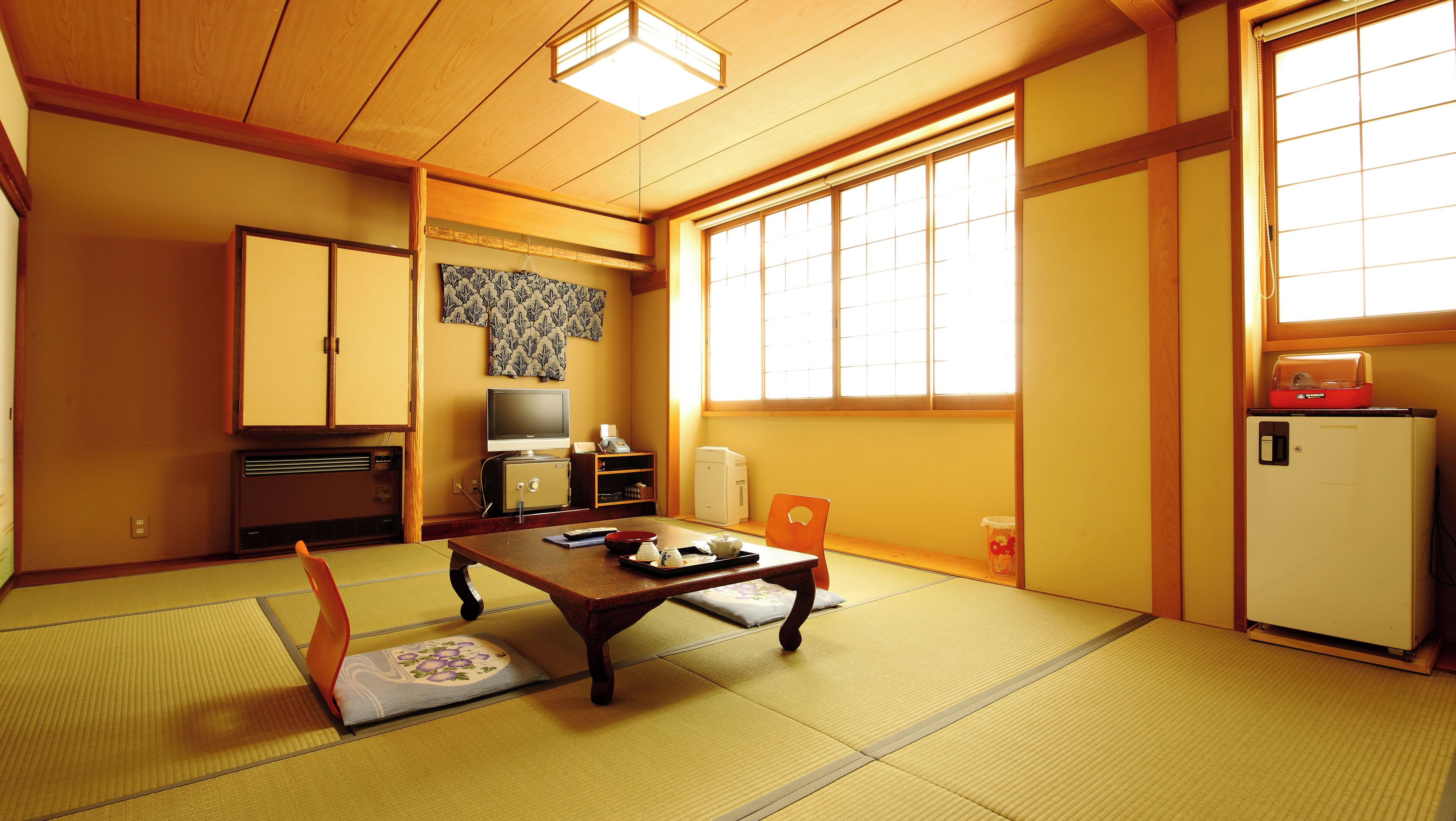 Une pièce de style japonais traditionnel, avec un sol recouvert de tatamis, une table basse, un téléviseur et un réfrigérateur.
