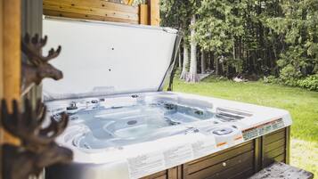 Un bain à remous avec une terrasse en bois et une forêt en arrière-plan.