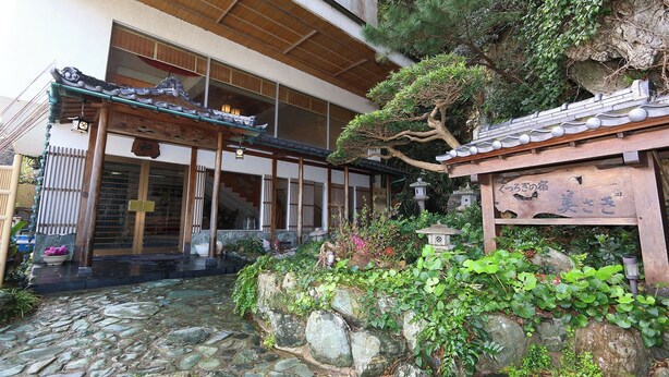 Een traditioneel Japans gebouw met een met stenen bestraatte binnenplaats, houten constructies en een kleine tuin met rotsen en planten.
