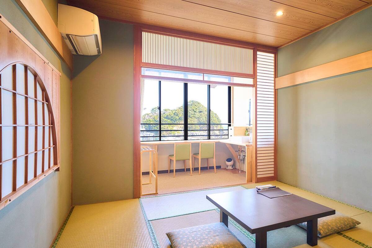Ein traditioneller japanischer Raum mit Tatami-Böden, einem niedrigen Tisch und einer Schiebetür, die auf einen Balkon führt.