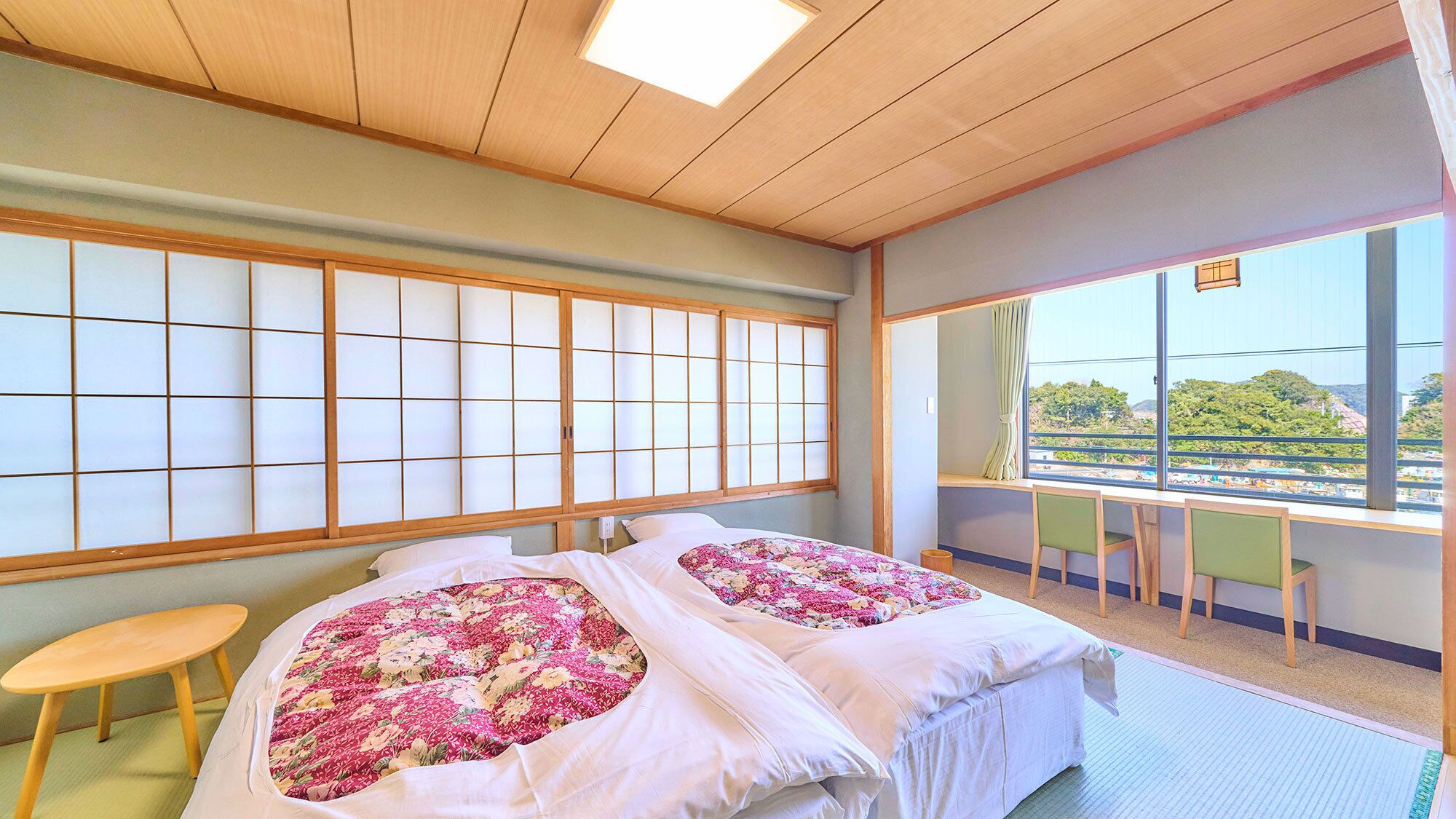 A room with two beds, a wooden ceiling, a large window with a view, and a small table.