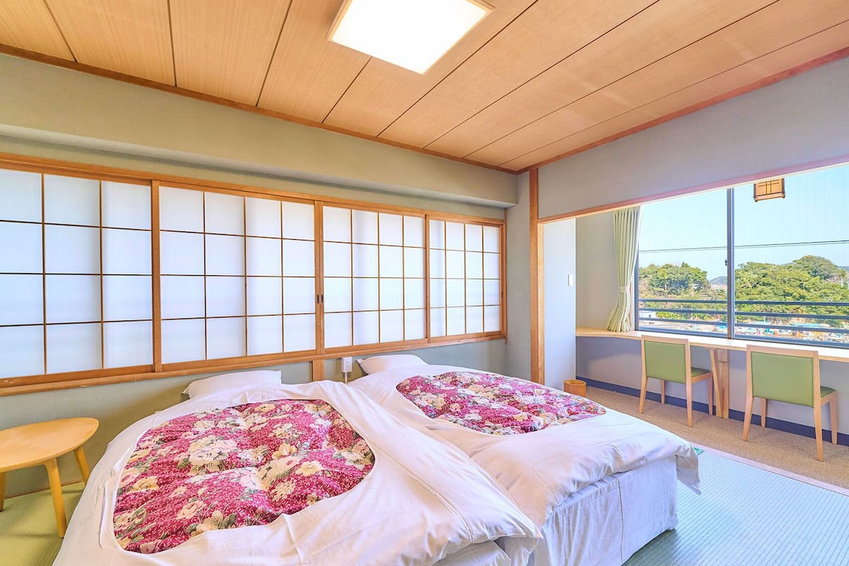A room with two beds, a wooden ceiling, a large window with a view, and a small table.