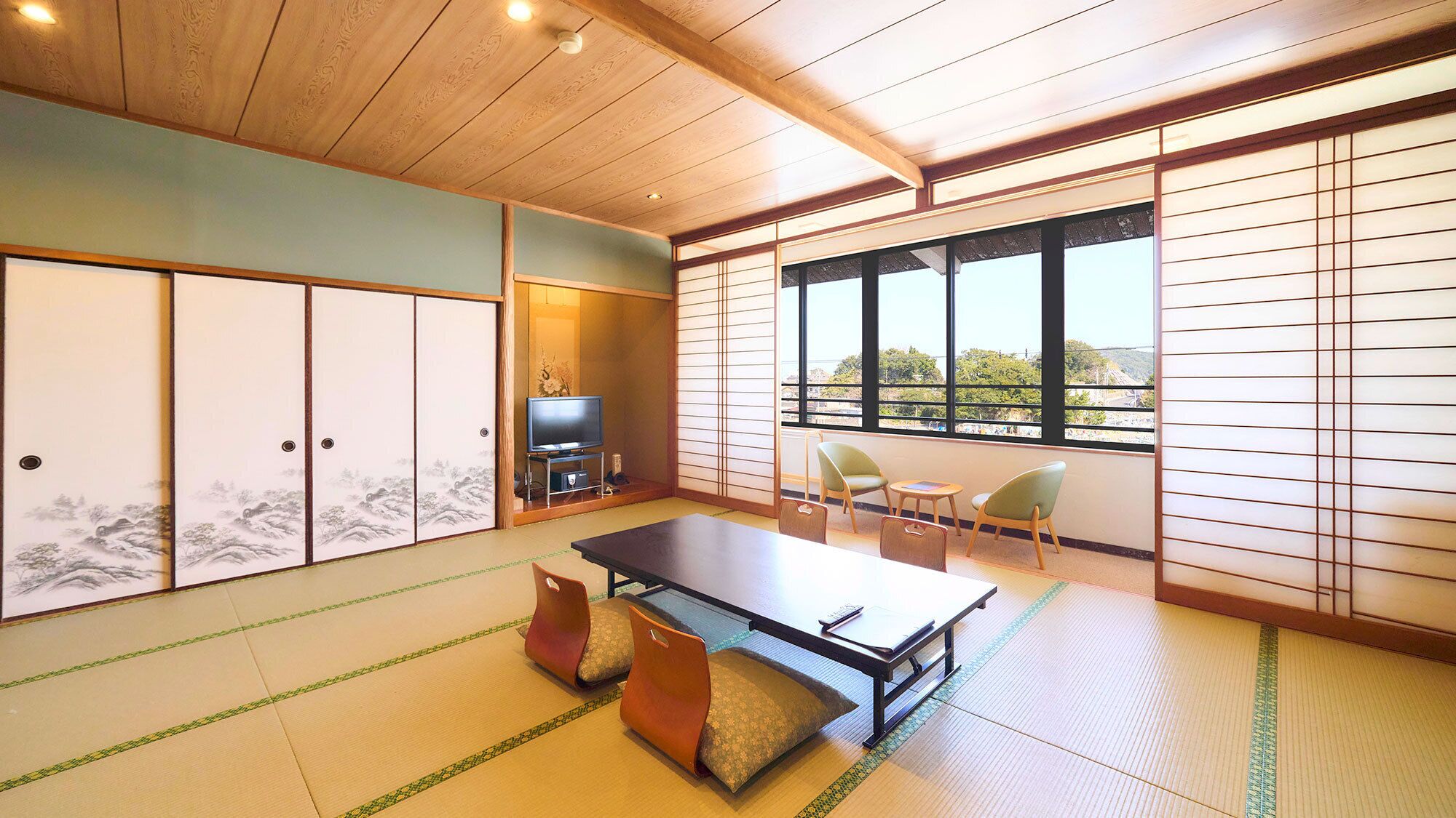 A traditional Japanese room with tatami flooring, a tatami mat table, a television, and sliding doors.