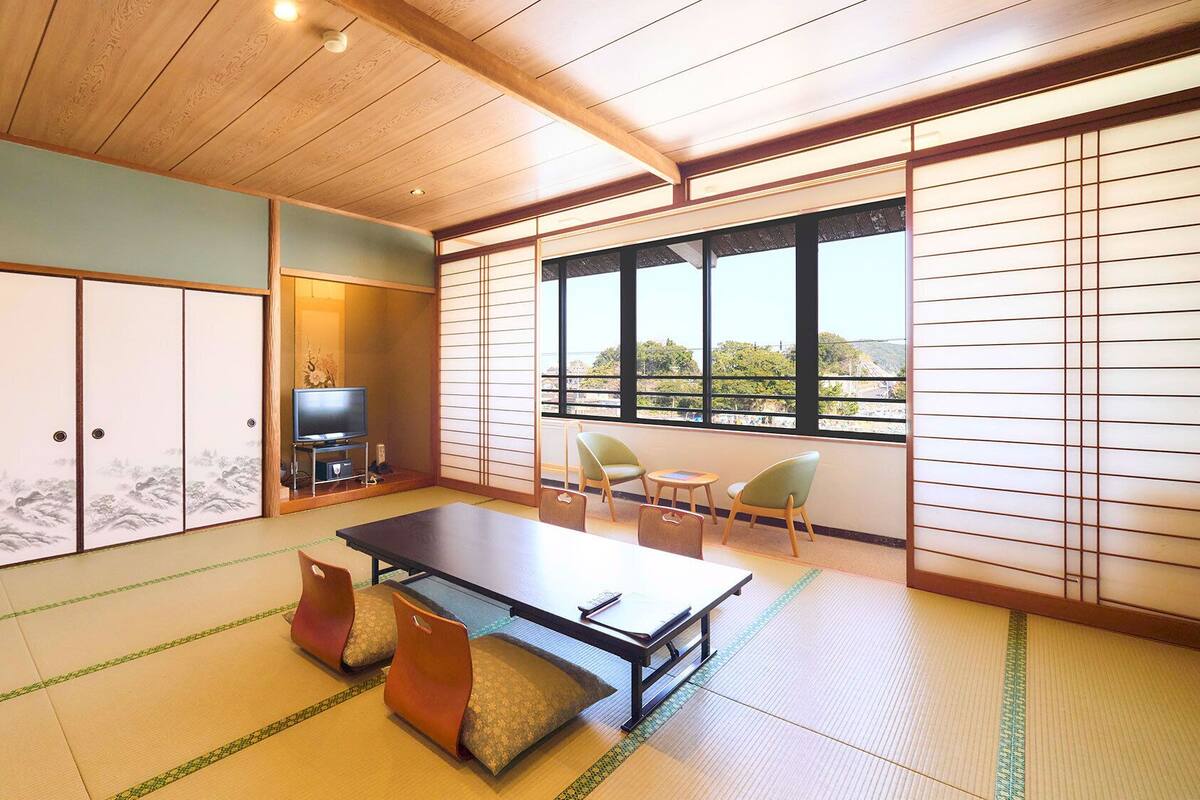 Ein traditioneller japanischer Raum mit Tatami-Boden, einem Tisch aus Tatami-Matten, einem Fernseher und gleitenden Schiebetüren.