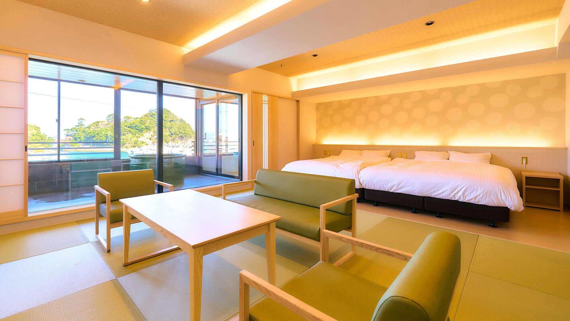 A hotel room with a large bed, a seating area with chairs, a table, and a view of a beach through large windows.