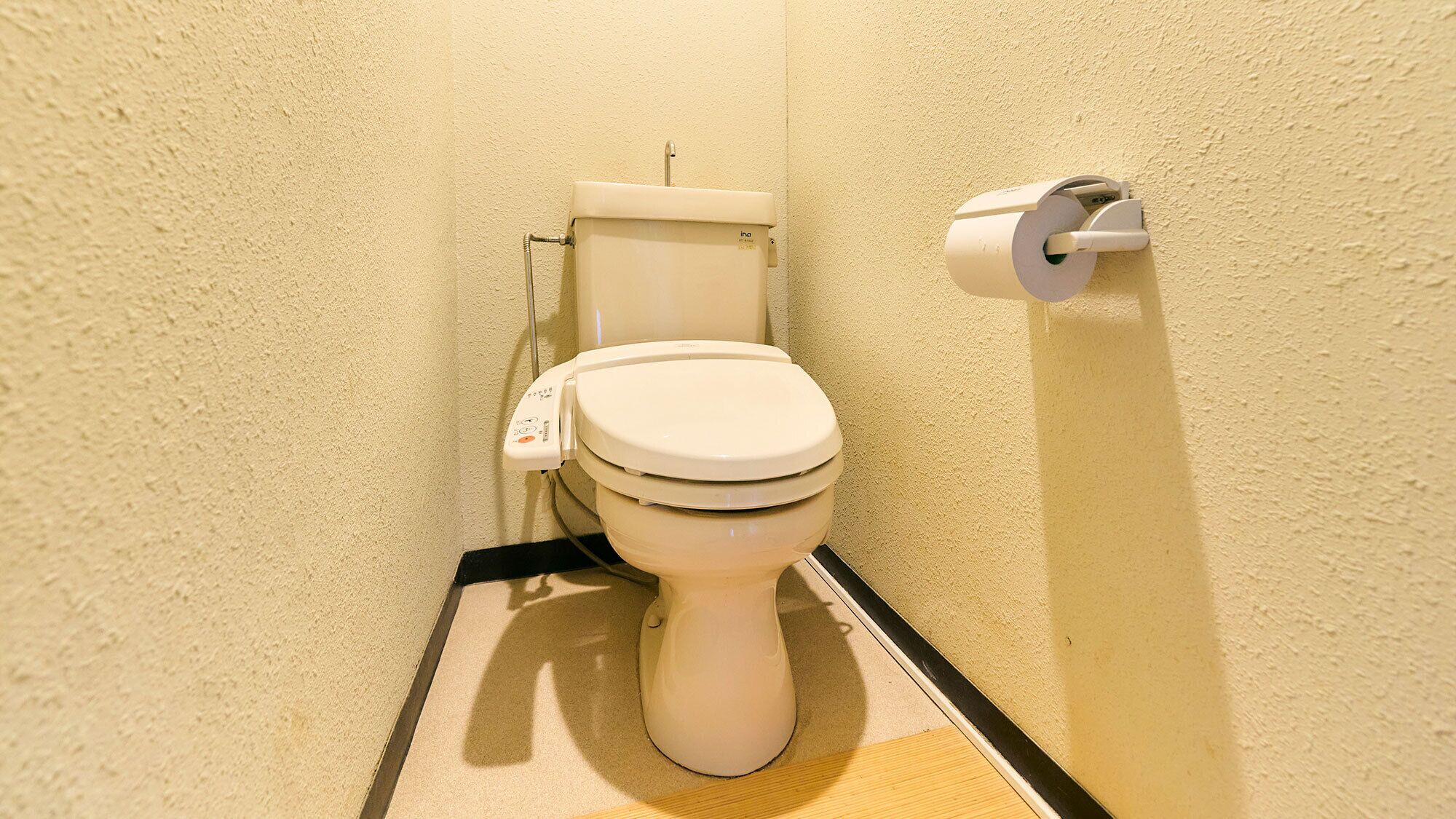 A toilet with a flush handle, a toilet paper holder, and a floor mat.