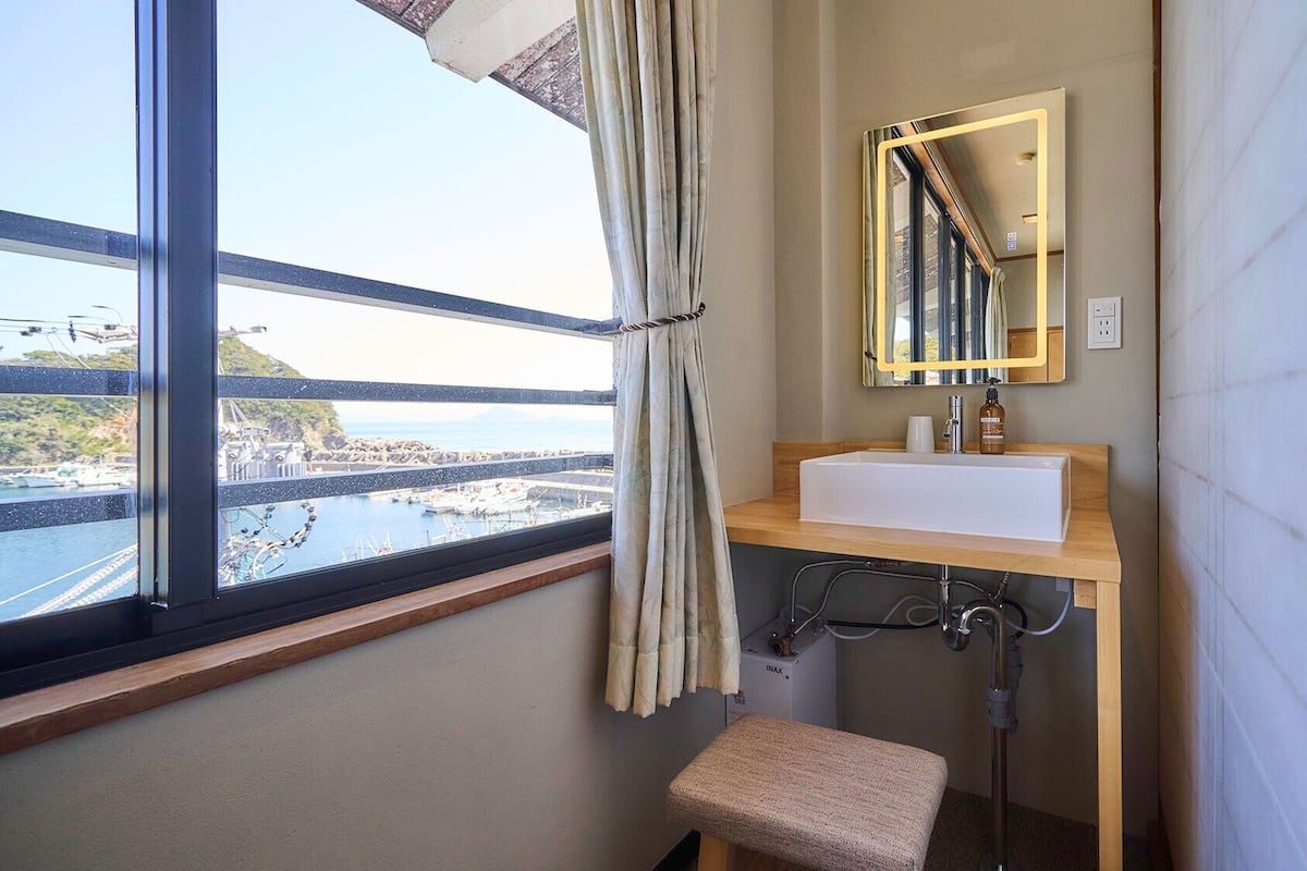A bathroom with a window, a sink, a mirror, and a shower.