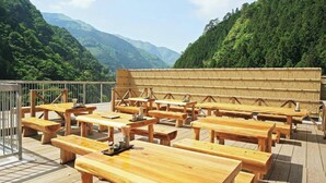 A wooden deck with tables and benches, surrounded by lush greenery and mountains. - Iya Bijin (Miyoshi)