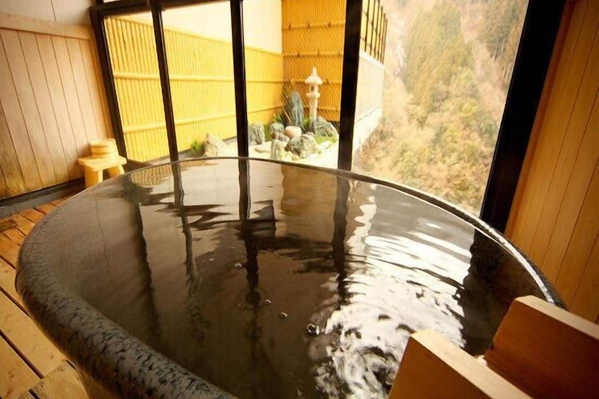 A hot tub with a wooden interior and a view of a mountainous landscape through large windows.