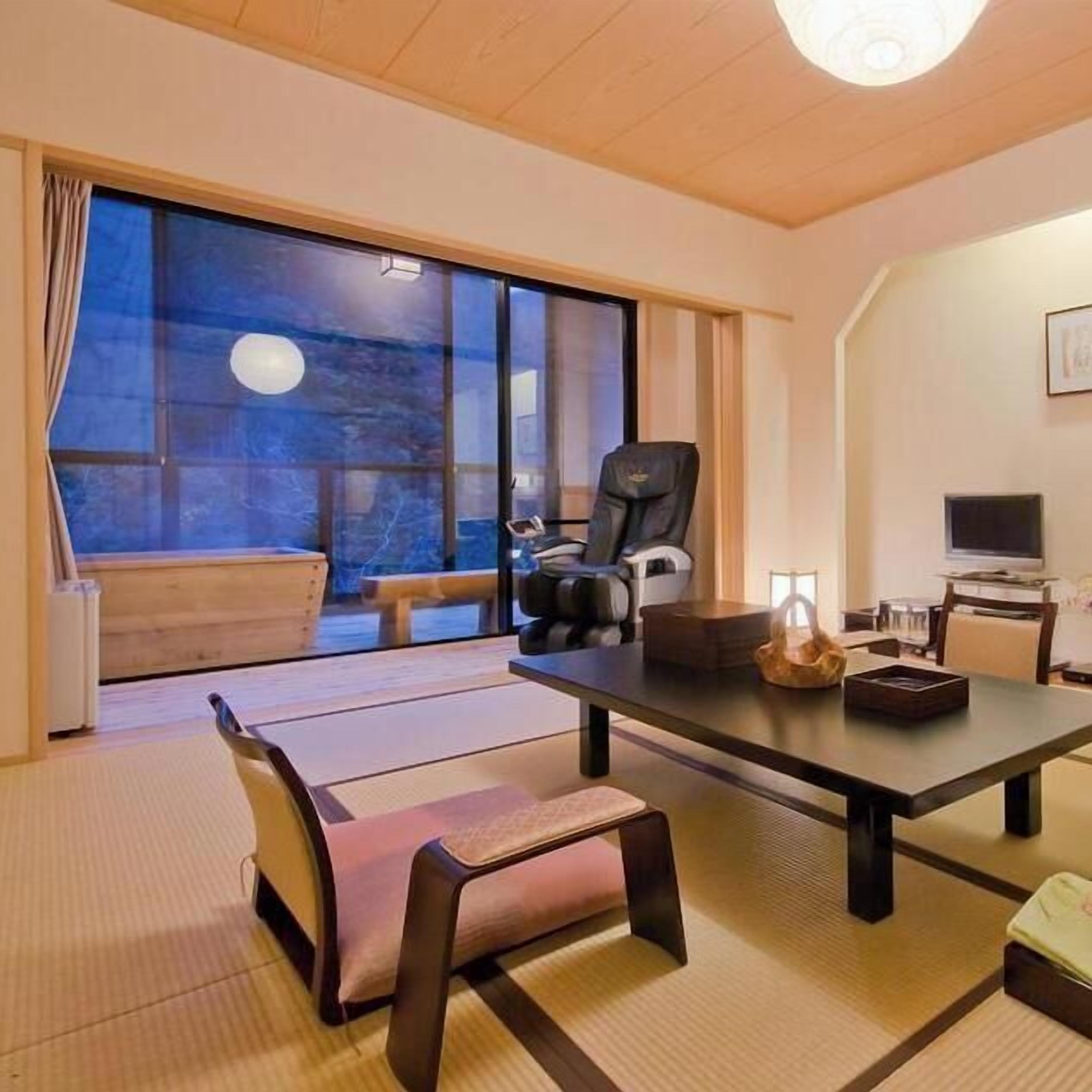 Une pièce avec des tatamis, une table basse, une chaise, un canapé, un téléviseur et une vue sur l’extérieur.