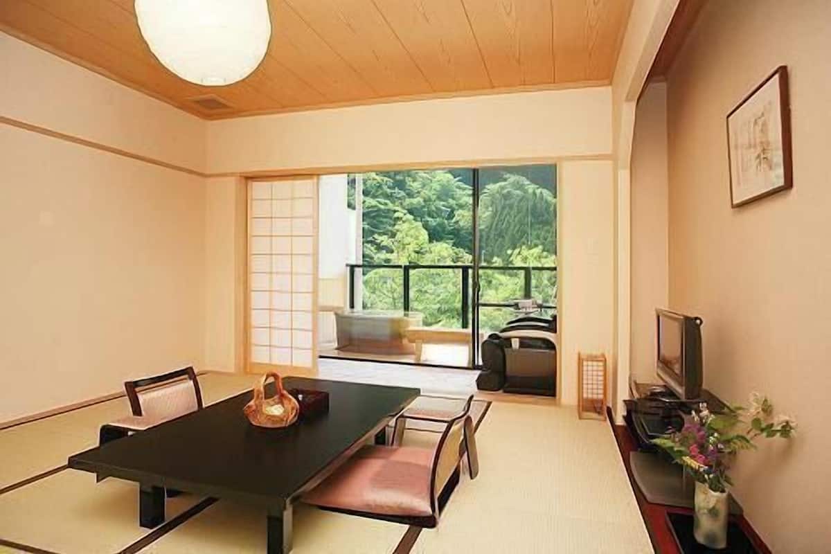A traditional Japanese-style room with tatami flooring, a low table, and a sliding door leading to a balcony with a view of greenery.