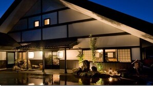 A traditional Japanese building with a tiled exterior, a covered entrance, and a small rock garden. - Iya Bijin (Miyoshi)
