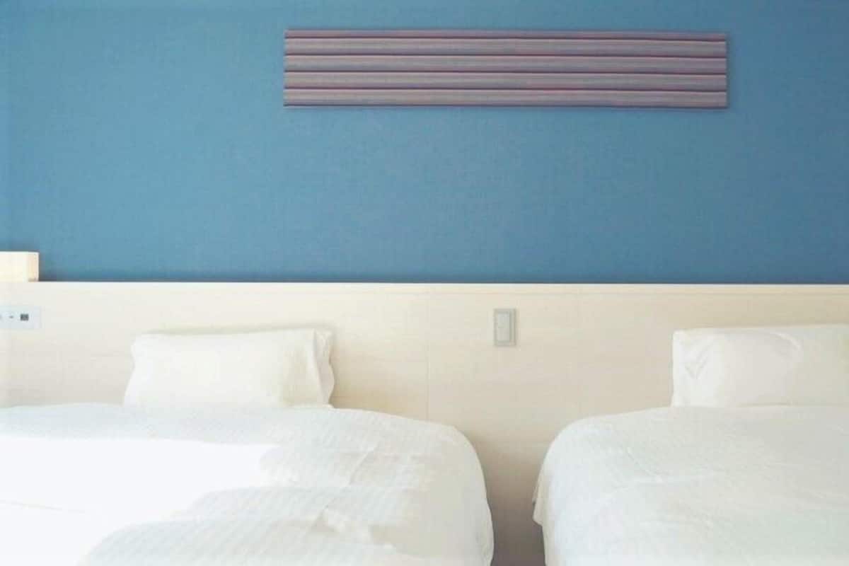 Habitación de hotel con dos camas, una pared azul y una lámpara horizontal.