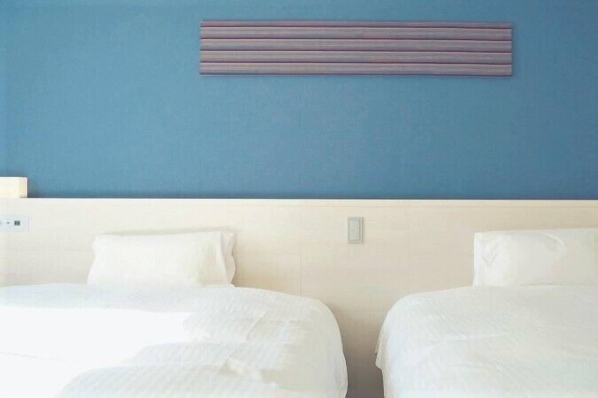 Habitación de hotel con dos camas, una pared azul y una lámpara horizontal.