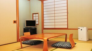 A traditional Japanese room with tatami flooring, a wooden table, two cushions, a television, and a white air conditioning unit. - Hotel Marine Palace Sanuki (Takamatsu)