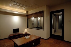 Una habitación de hotel con piso de madera, un escritorio con lámpara, un televisor y un espejo grande.