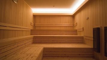A sauna with wooden benches and steps, a clock on the wall, and a wooden door.