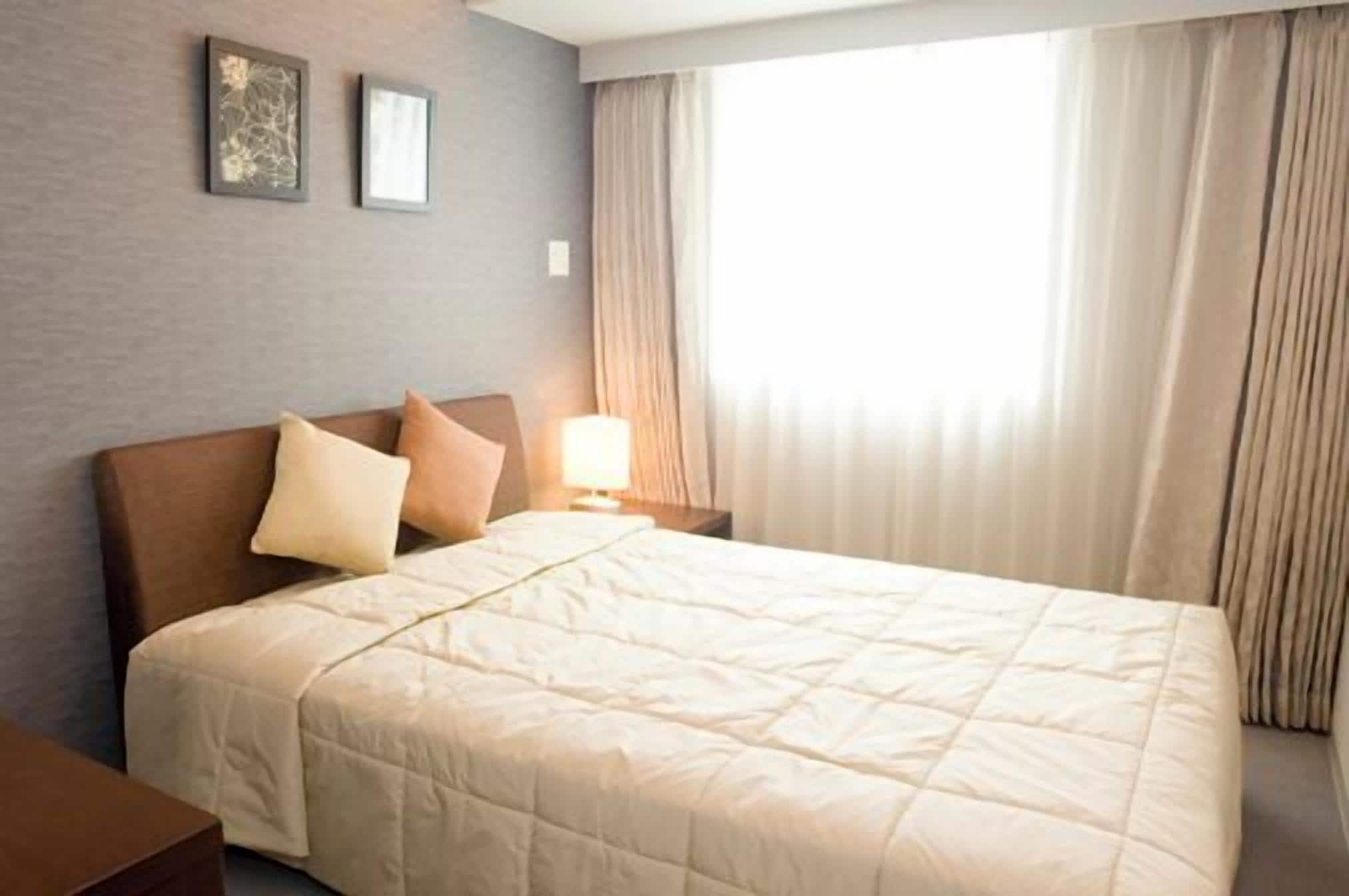 A hotel room with a bed, a nightstand, a lamp, and a window with curtains.