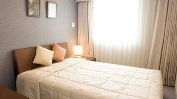 A hotel room with a bed, a nightstand, a lamp, and a window with curtains.