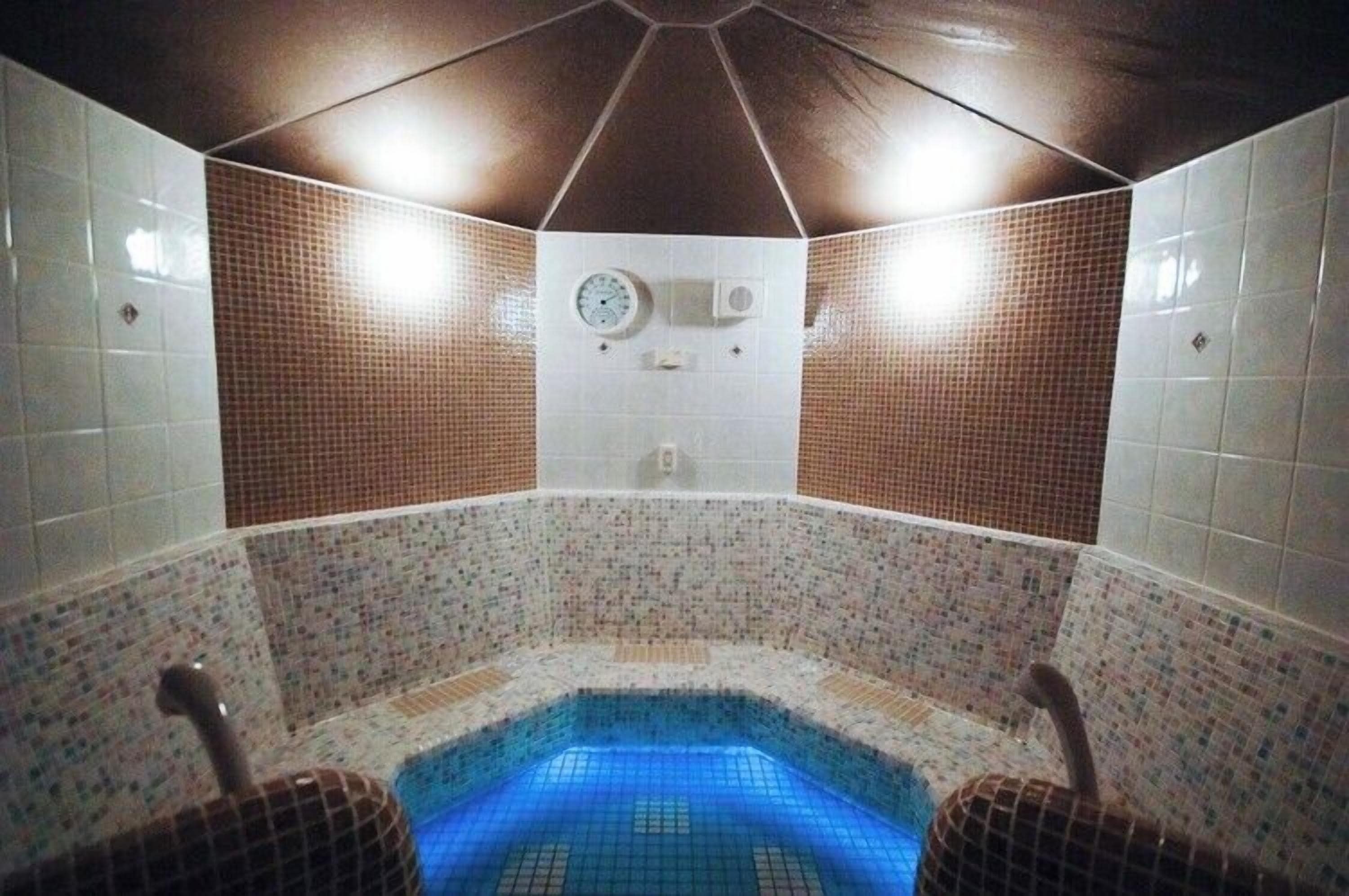 A hot tub with a tiled interior, a clock on the wall, and a ceiling with recessed lighting.