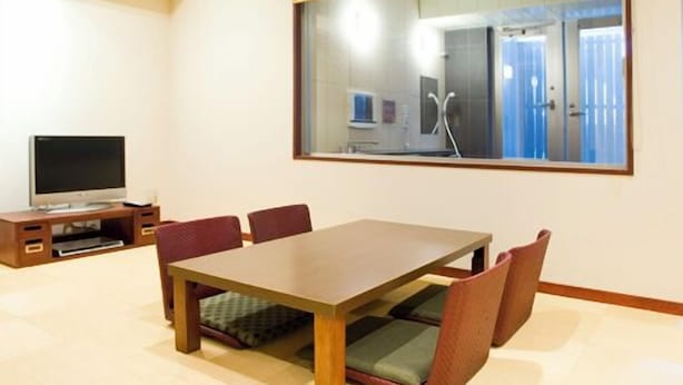 Une chambre d’hôtel avec une table à manger en bois, des chaises rembourrées, un téléviseur à écran plat et un grand miroir qui reflète la pièce.