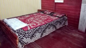A small, single-bed room with a patterned bedspread, a red wall, and a window. - Wooden Paracosm & Resort (Thissamaharama)