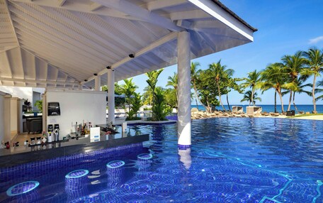 A pool area with a bar, palm trees, and a view of the ocean.