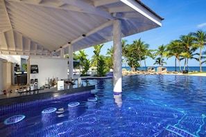 Un espace piscine doté d’un bar, de palmiers et offrant une vue sur l’océan.