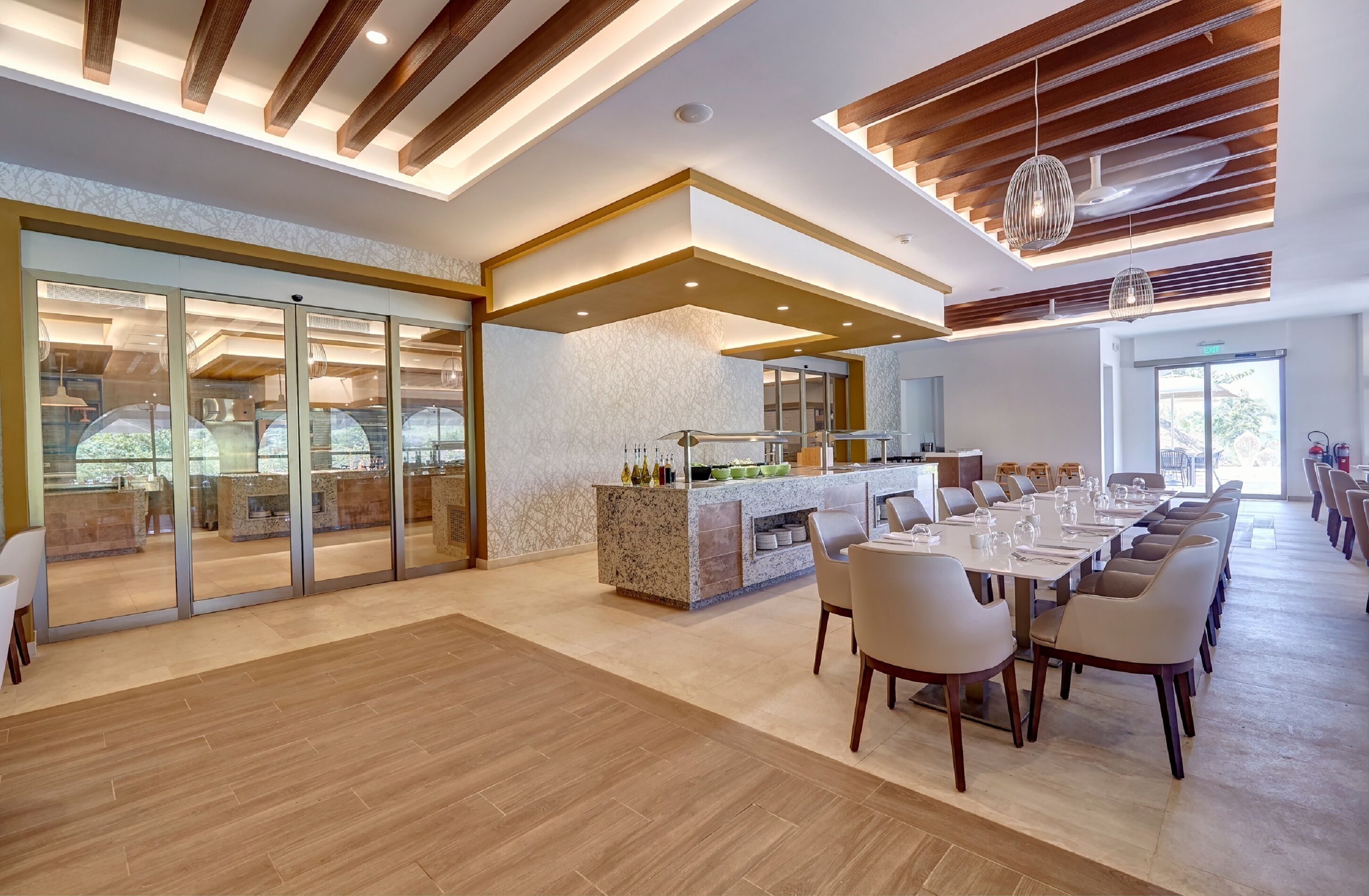 A modern hotel lobby with a central bar, seating area, and glass doors leading to a dining space.