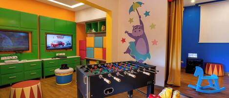 Una habitación de colores vivos con una mesa de fútbol de mesa, una televisión y un mural en la pared.