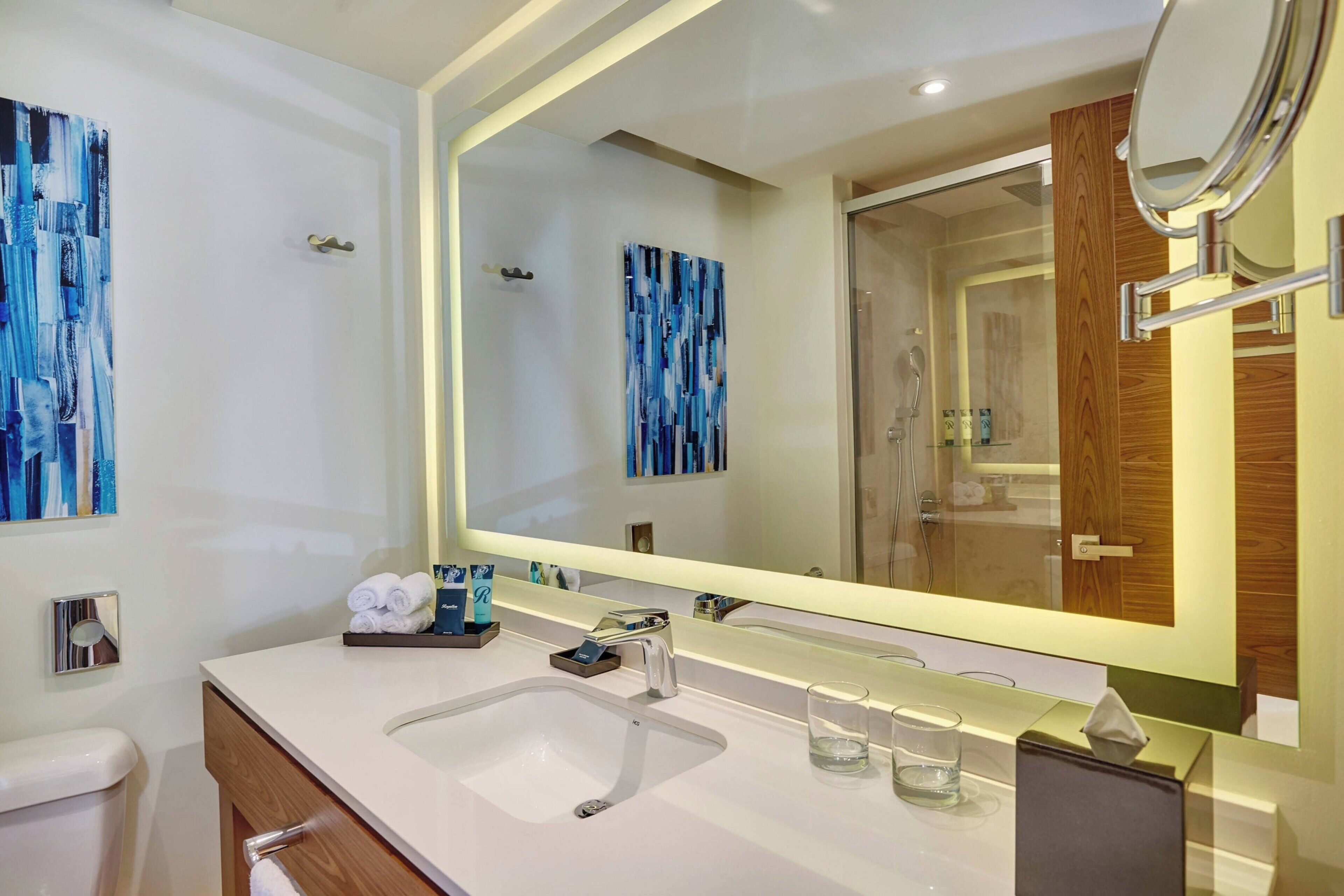 A modern bathroom with a large mirror, a sink, and a shower.