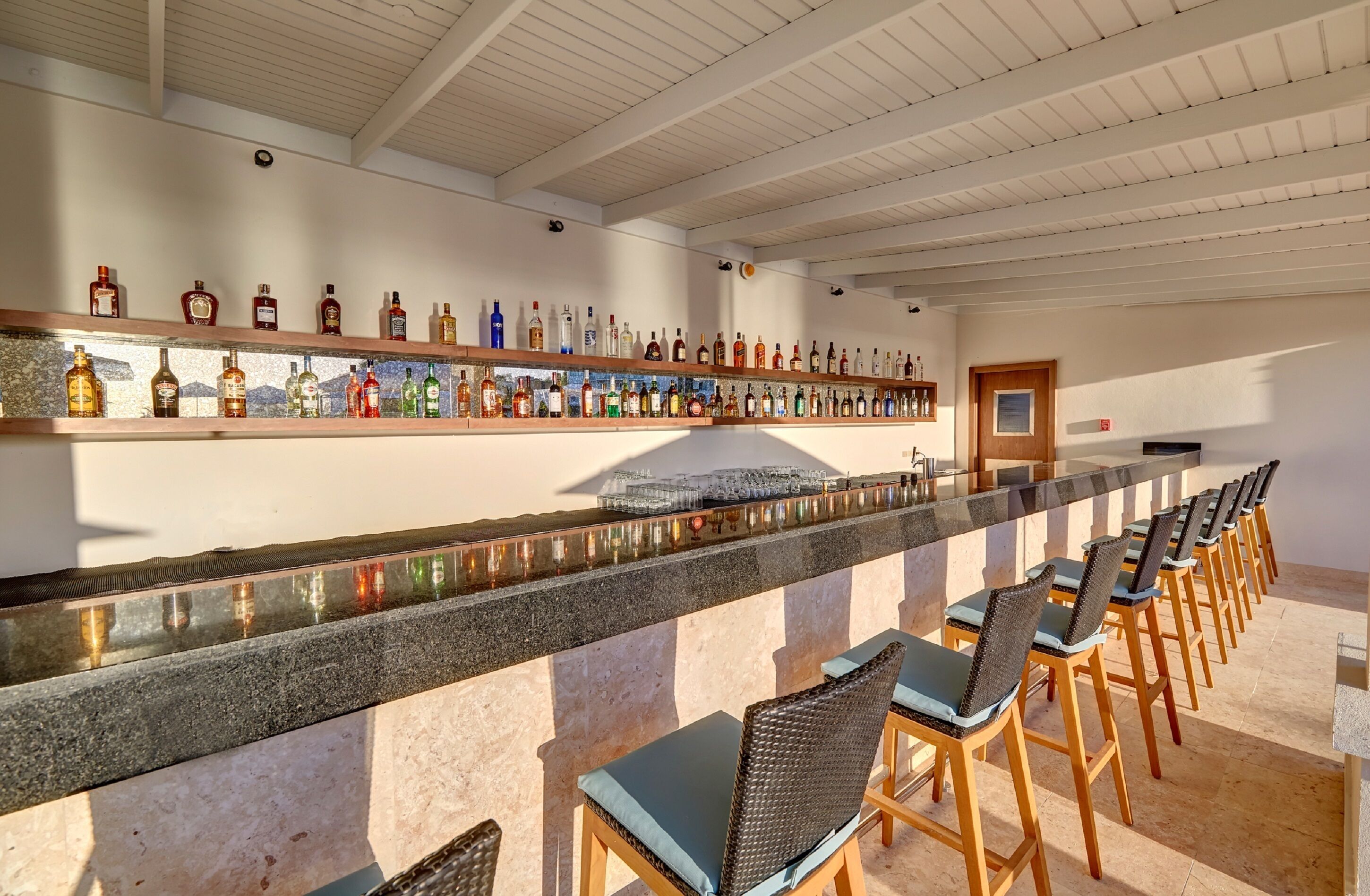 A bar area with a long counter, multiple liquor bottles, and several bar stools.