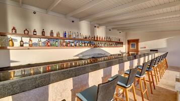 A bar area with a long counter, multiple liquor bottles, and several bar stools.