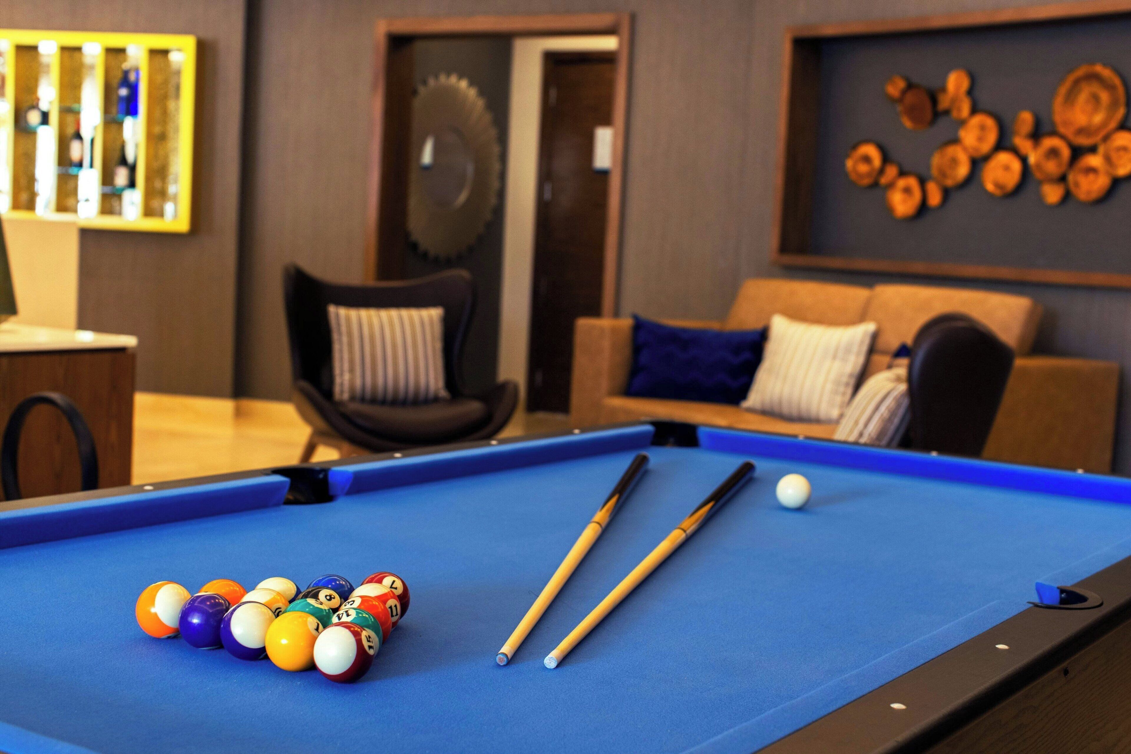 A pool table with billiard balls and cues, a sofa with cushions, and a wall with decorative wooden plates.
