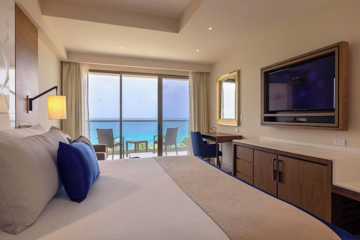 A hotel room with a large bed, a desk, a television, and a view of the ocean.