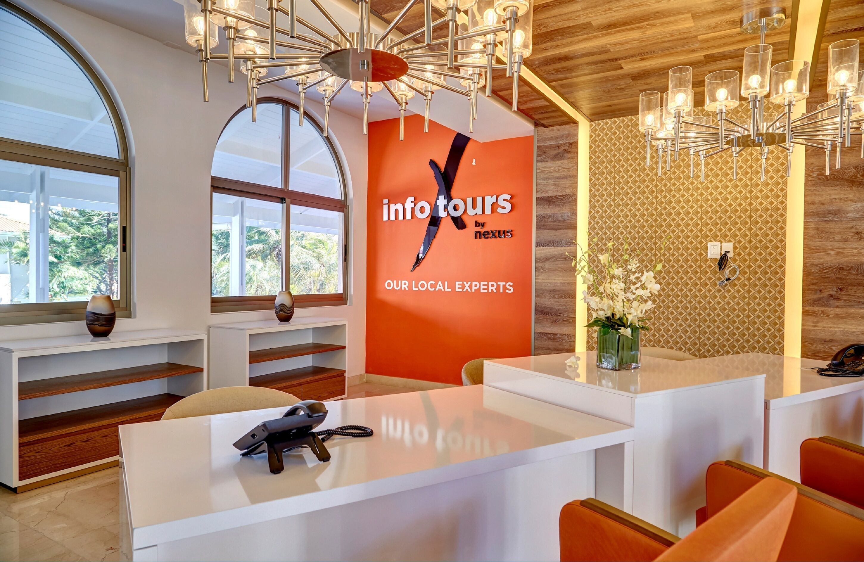 A modern reception area with a large desk, a chandelier, and a wall with a logo.
